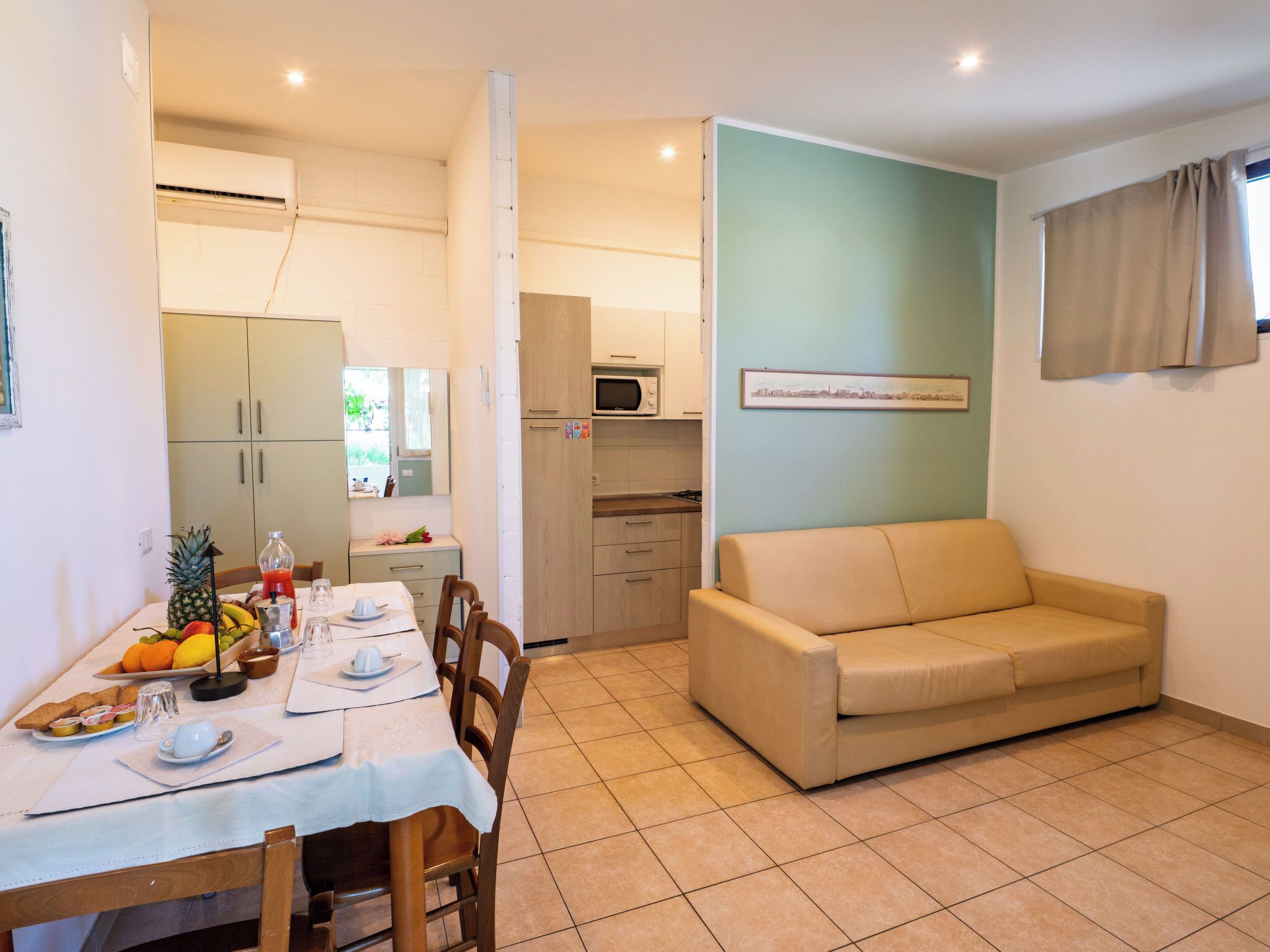 A dining area with a table set for two, a sofa, and a kitchenette in the background.