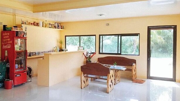 A spacious room with a wooden table and benches, a red Coca-Cola refrigerator, and large windows offering a view of greenery. - RedDoorz @ Reana Seaside Pensione House Guindulman (Guindulman)