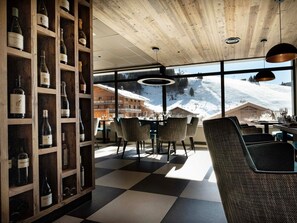 Un restaurant à l’intérieur en bois, de grandes fenêtres donnant sur un paysage de montagne enneigée et un présentoir à vin contenant différentes bouteilles.