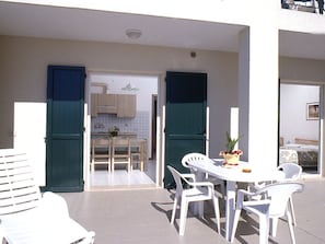 A patio area with a table and chairs, a small kitchen in the background, and a door leading to another room. - Albatros by Interhome (Caorle)