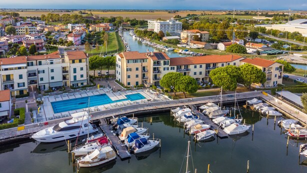 A marina with boats docked, a swimming pool, and buildings with balconies. - Albatros by Interhome (Caorle)