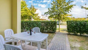 Un patio con una mesa y sillas, una botella de vino, y vistas a un árbol y un seto.