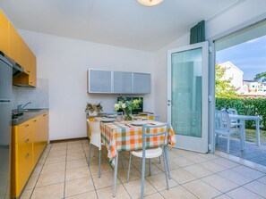 A compact kitchen with yellow cabinets, a dining table set for four, and a sliding glass door leading to an outdoor area. - Robinia/Pinetine by Interhome (Caorle)