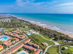 An aerial view of a coastal resort with multiple buildings, a large swimming pool, and a well-maintained beachfront. - Robinia/Pinetine by Interhome (Caorle)