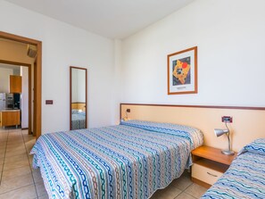 A hotel room with a bed, a bedside table with a lamp, a mirror, and a framed picture on the wall. - Robinia/Pinetine by Interhome (Caorle)
