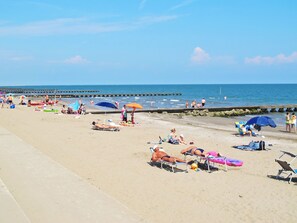 Una playa con gente tomando el sol, sombrillas y sillas de playa.