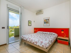 Un dormitorio con cama, cabecera roja, mesita de noche, ventana con vistas y un equipo de aire acondicionado.