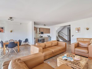 A spacious living area with a sofa, a coffee table, and a dining table with chairs. A kitchen with modern appliances is visible in the background. - Villas Odalys Collection Orée de Milady by Interhome (Biarritz)