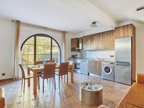 Una cocina moderna con armarios de madera, un refrigerador de acero inoxidable, una lavadora y un comedor con un amplio ventanal.