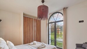 Un dormitorio con una cama grande, un armario de madera, un sillón gris y un ventanal con vistas a la vegetación.