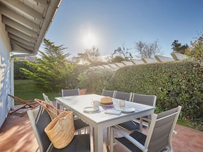 En udendørs terrasse med et bord dækket til to, omgivet af stole, en flettet kurv og et par solbriller.