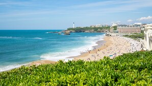 Una playa con un faro, una orilla arenosa y edificios al fondo.
