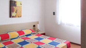Uma cama bem arrumada com um edredom colorido, uma mesa de cabeceira com abajur e um quadro na parede.