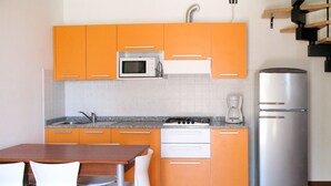 Cozinha compacta com armários laranjas, micro-ondas branco, fogão, máquina de café e geladeira. Há uma mesa de jantar com cadeiras.