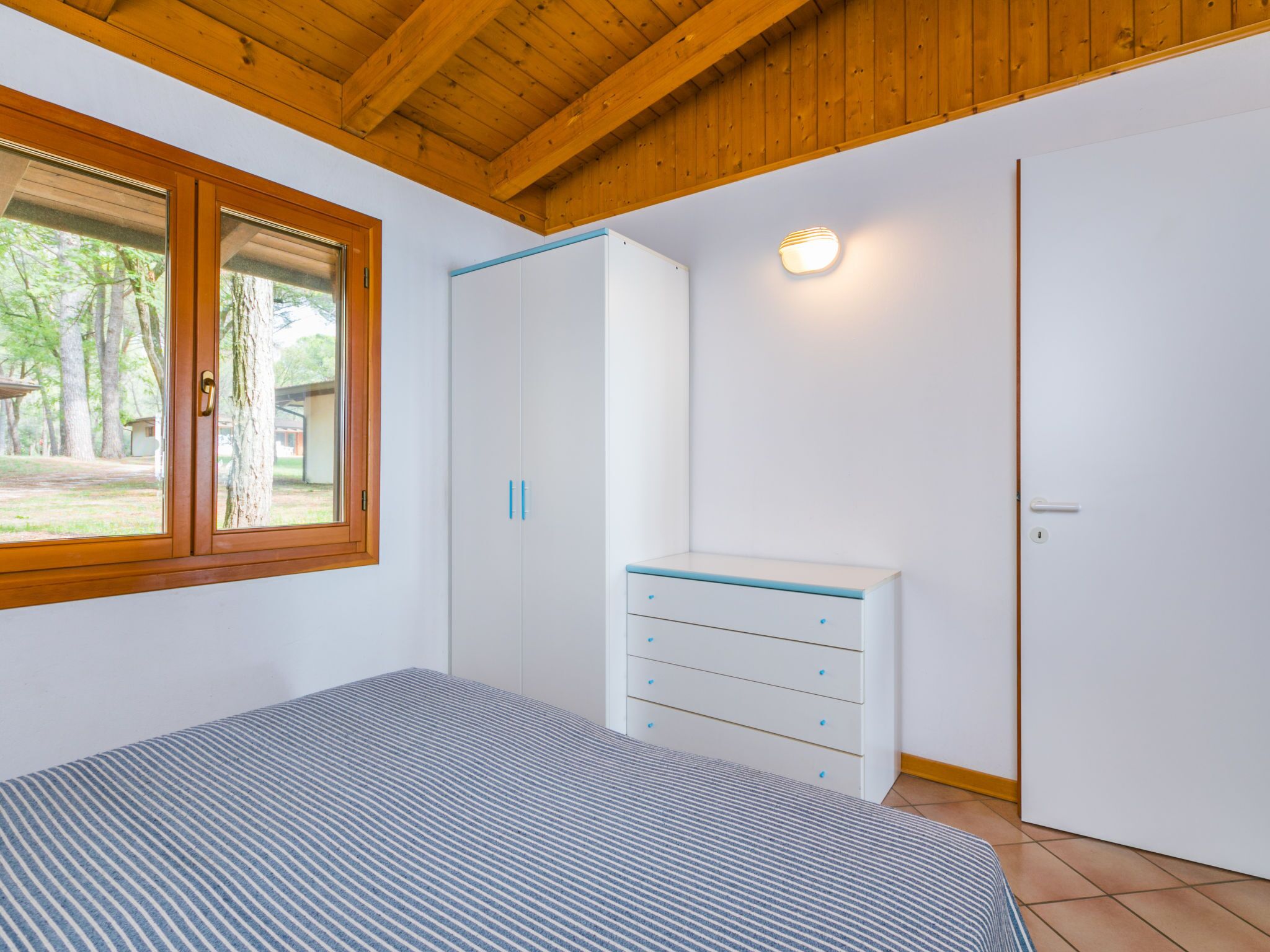 Un dormitorio con cama, armario, tocador y ventana con vistas a árboles.