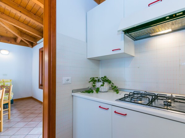 Une cuisine avec des meubles blancs, une cuisinière à gaz et une poignée rouge.