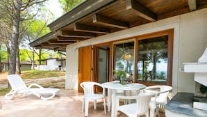 Eine Terrasse im Freien mit weißen Kunststoffstühlen und einem runden Tisch, umgeben von einer Holz-Pergola und Glastüren zu einem überdachten Bereich.