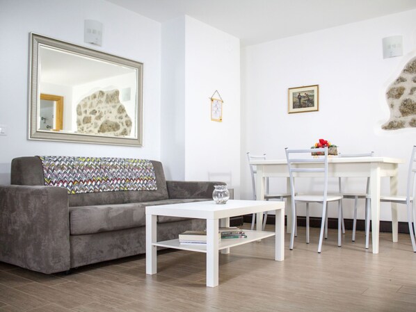 A modern living room with a grey sofa, a white coffee table, and a dining area with a white table and chairs.