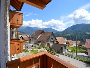 A balcony with a wooden railing overlooking a village with traditional houses and a mountain backdrop. - Casa Rasat by Interhome (Ovaro)