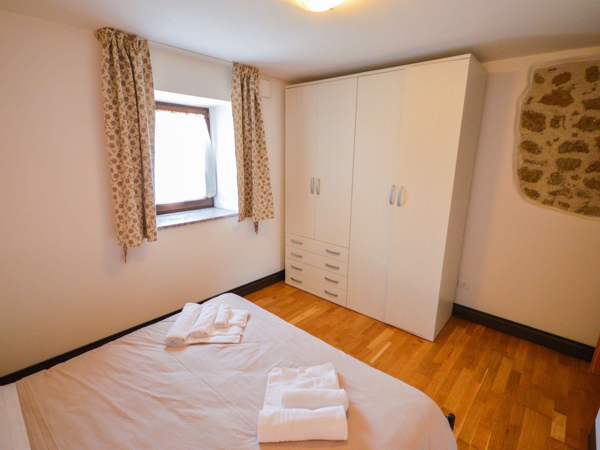 A bedroom with a bed, a wardrobe, and a window with curtains.