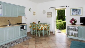 A kitchen with teal cabinets, a dining table with chairs, a clock, and a door leading to a garden. - I Cortivi by Interhome (Garda)