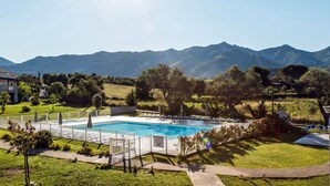 Une piscine entourée d’une clôture blanche, bordée de verdure et avec une chaîne de montagnes en toile de fond.