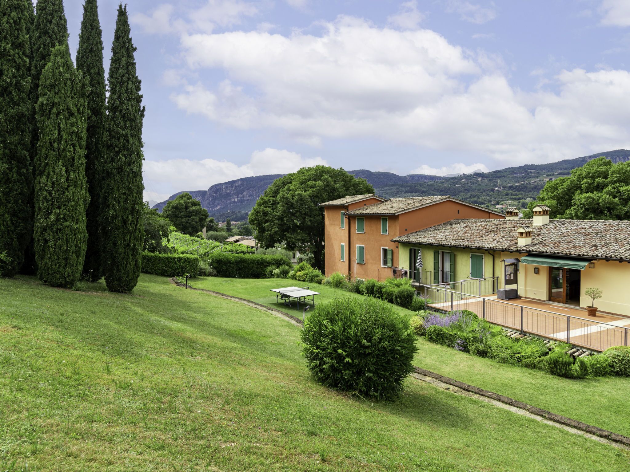 A villa with a well-maintained lawn, a tennis court, and a view of mountains in the background.