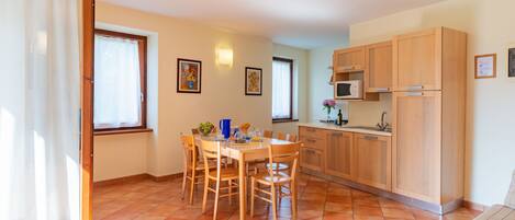 A compact kitchen with wooden cabinets, a dining table with chairs, and a tiled floor.