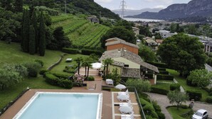 Ein Poolbereich mit Liegestühlen und Sonnenschirmen, umgeben von gepflegten Gärten und Blick auf eine Berglandschaft.