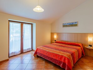 A bedroom with a bed, a window with curtains, a painting on the wall, and a ceiling light.