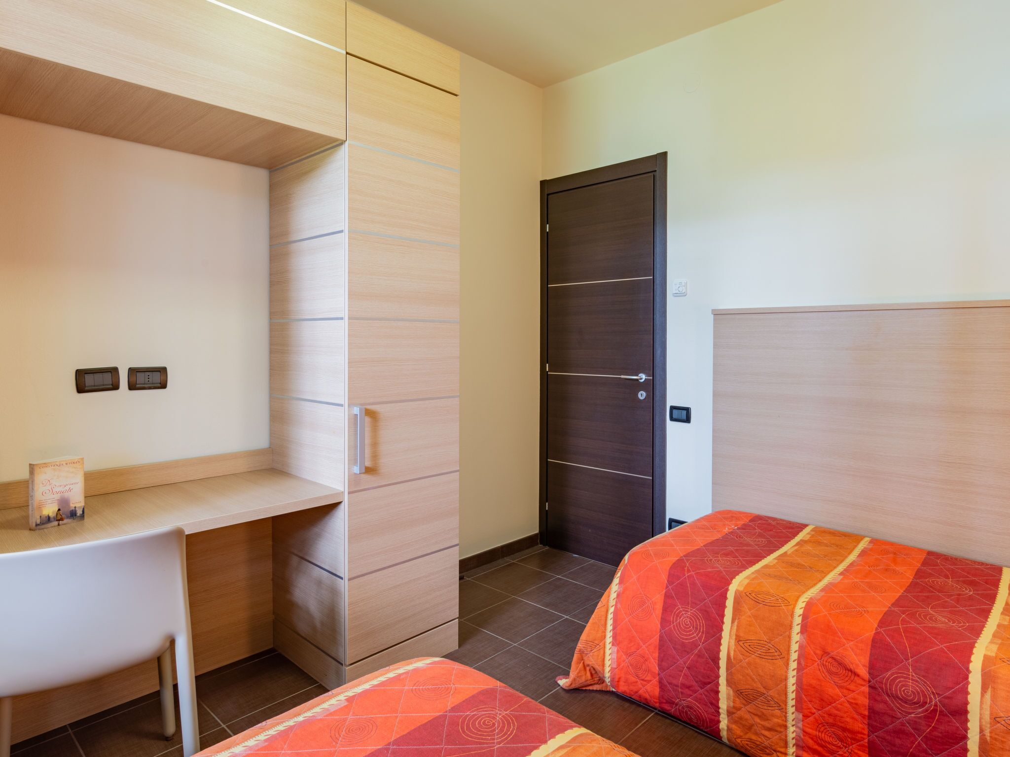 A hotel room with a desk, two beds, a wardrobe, and a door.