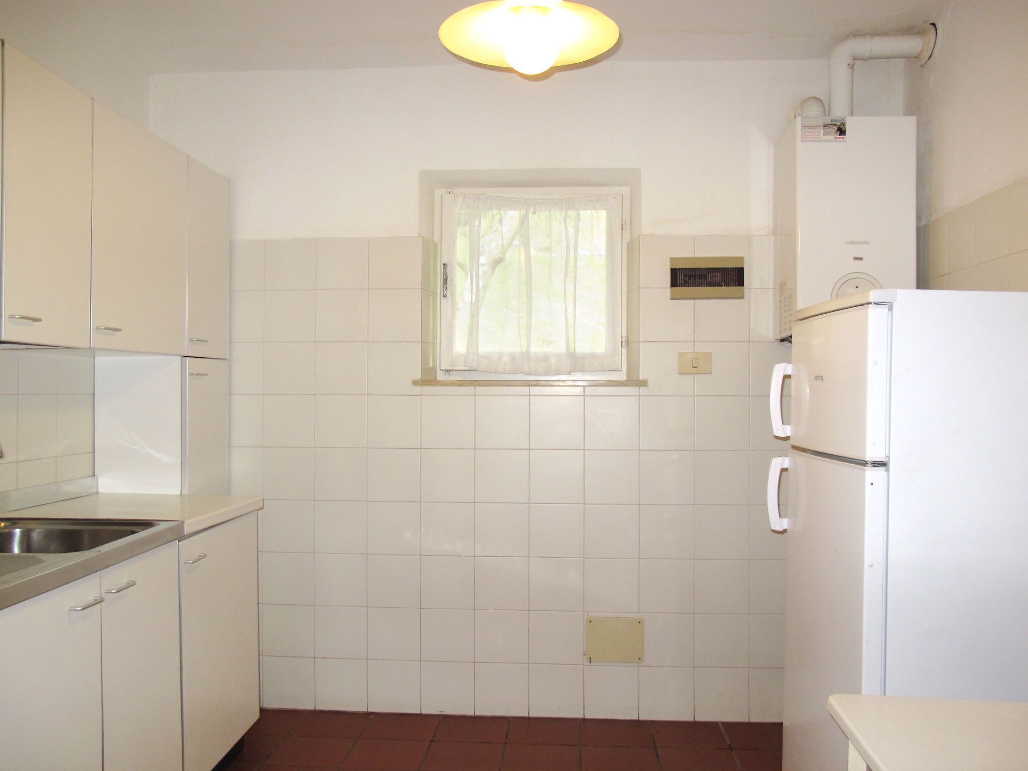 A kitchen with white cabinets, a window, a built-in oven, and a refrigerator.