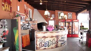 Zona de bar con mostrador, estantes con botellas, horno para pizzas y refrigerador de Coca-Cola.