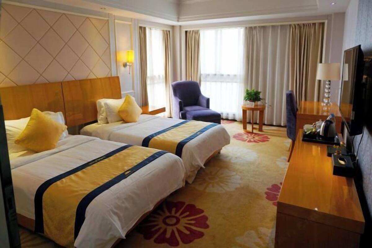 A hotel room with two beds, a desk, a chair, a TV, and a window with curtains.