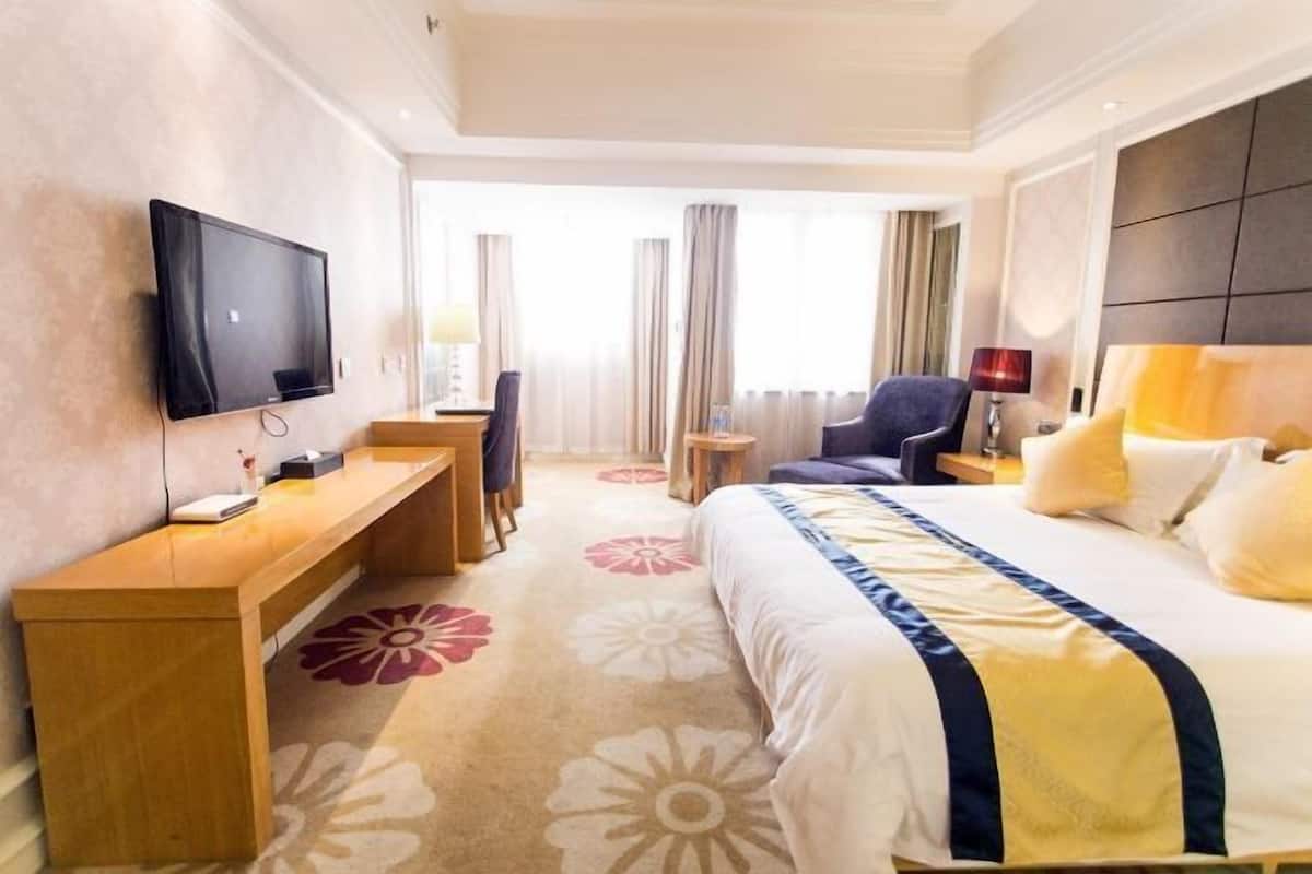 Quarto de hotel com cama, escrivaninha, cadeira, televisão e janela com cortinas.