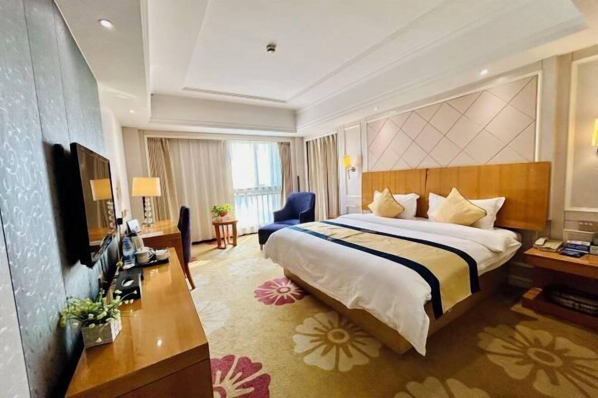 A hotel room with a large bed, a desk with a computer, a chair, a TV, and a window with curtains.