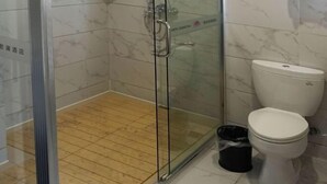 A bathroom with a glass shower enclosure, a toilet, and a trash bin. - Green Journey Inn (Suzhou)