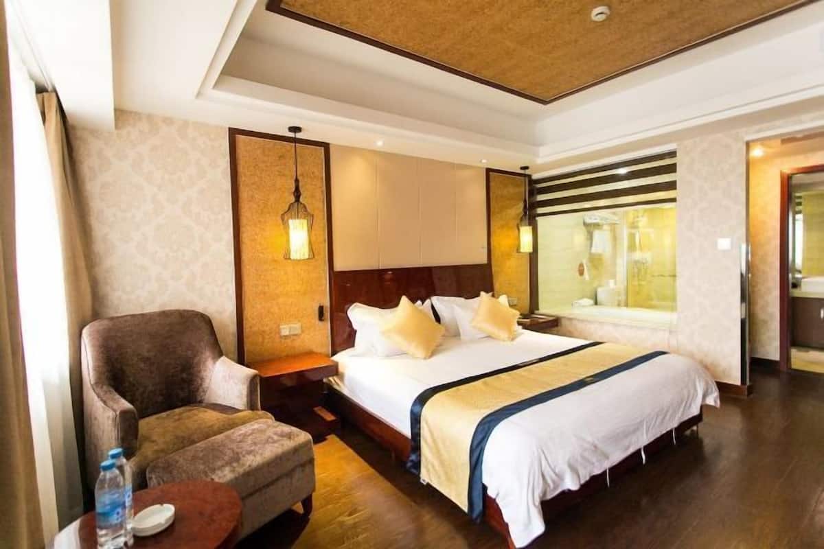 Quarto de hotel com uma cama, uma cadeira, uma mesinha com uma garrafa e um espelho.