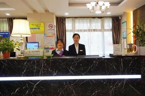 A hotel reception desk with a marble top, a computer, a telephone, and a plant. - Green Journey Inn (Suzhou)