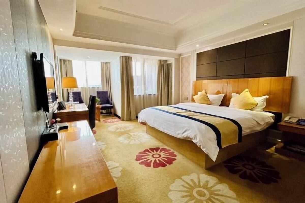 A hotel room with a large bed, a desk, a chair, and a TV.