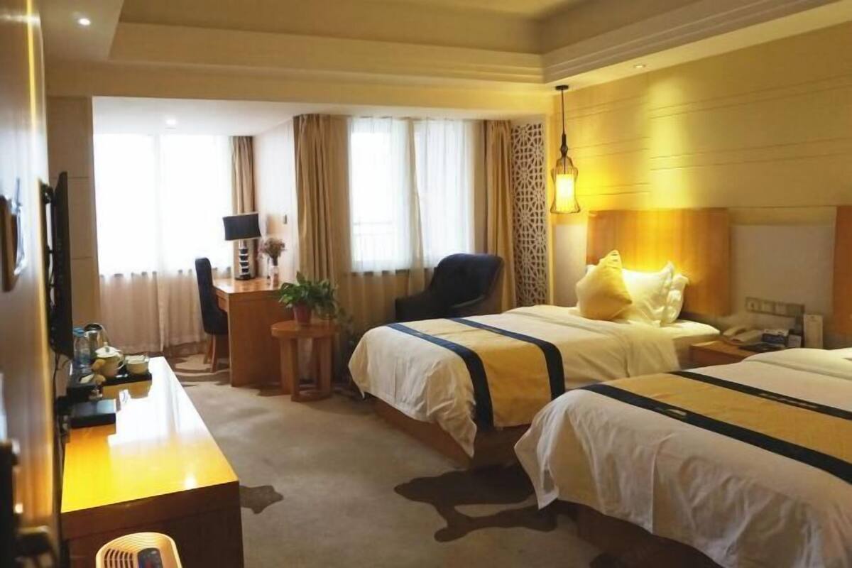 Quarto de hotel com duas camas, uma escrivaninha, uma cadeira, uma televisão e um abajur.