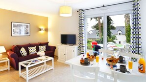 Una sala de estar con sofá, televisión y comedor con alimentos para el desayuno.