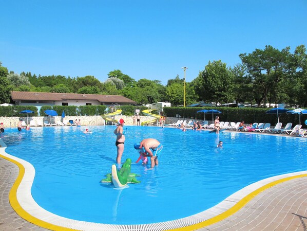 Una piscina con agua cristalina azul, rodeada de sillas de descanso y sombrillas.