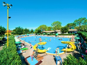 Uma grande piscina ao ar livre rodeada por vegetação exuberante e um céu azul límpido.