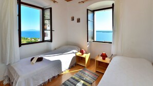Una habitación con dos camas, amplias ventanas con vistas al océano, techo de madera y una pequeña mesa con una lámpara.