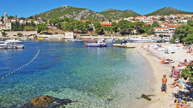 A coastal town with clear waters, boats, and a beach with people.
