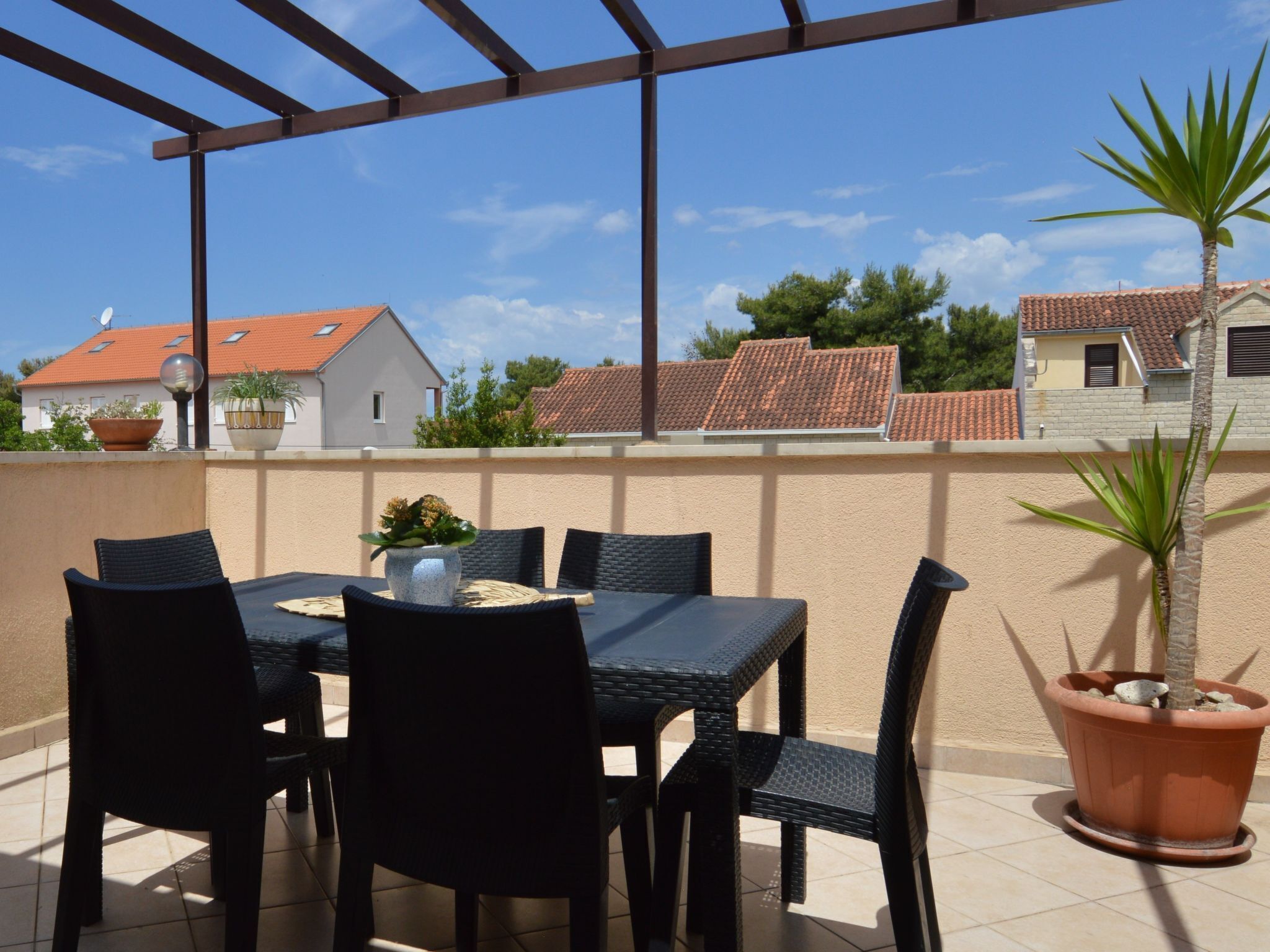 An outdoor patio with a table and chairs, potted plants, and a view of neighboring houses.