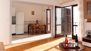 Ein modernes Wohnzimmer mit Holzboden, einer Essecke mit Tisch und Stühlen, einer Küche mit weißen Geräten und einem Balkon mit Ventilator.