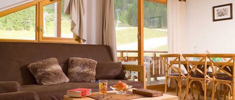 Una sala de estar acogedora con un sofá marrón, una mesa de centro de madera y un comedor con sillas y mesa de madera.