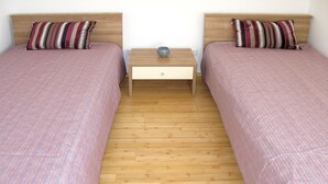 Quarto duplo com duas camas, cada uma com roupa de cama listrada, uma cabeceira de madeira e uma mesa de cabeceira com abajur.